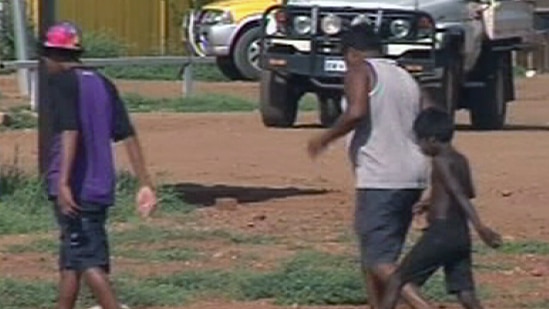 Three Aboriginal boys walk across dirt ground