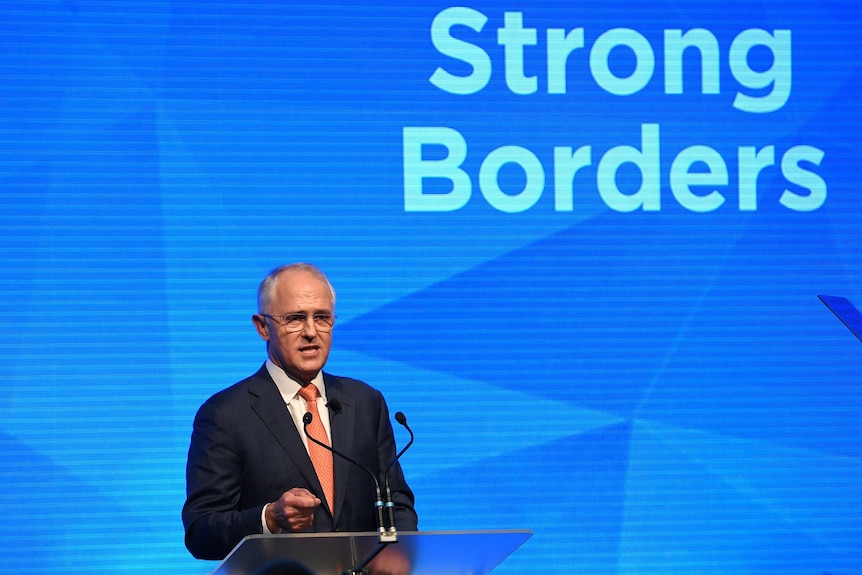 Prime Minister speaks at a podium in front of a screen saying strong borders.