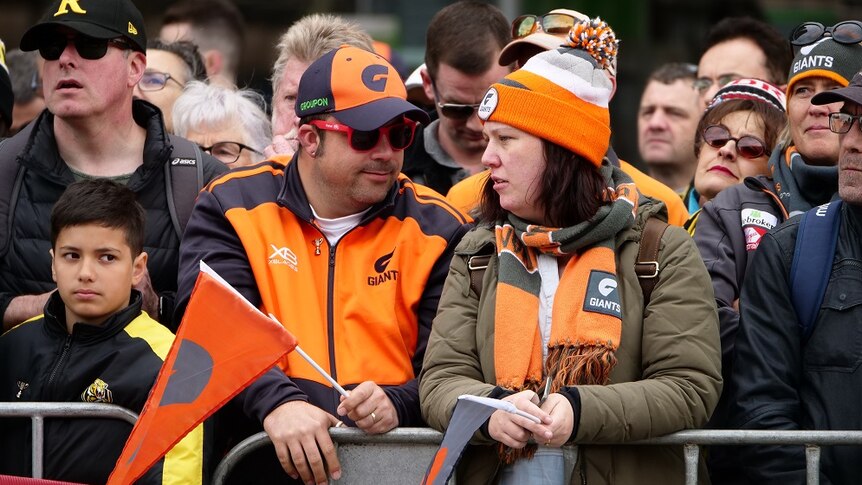A group of AFL fans wearing GWS Giants merchandise look on as the grand final parade takes place.