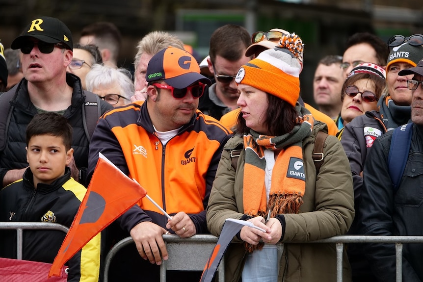A group of AFL fans wearing GWS Giants merchandise look on as the grand final parade takes place.