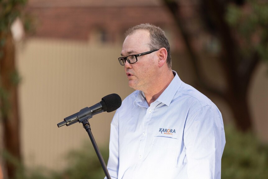 A mining executive speaking behind a microphone and podium at a memorial service for mining industry workers.  