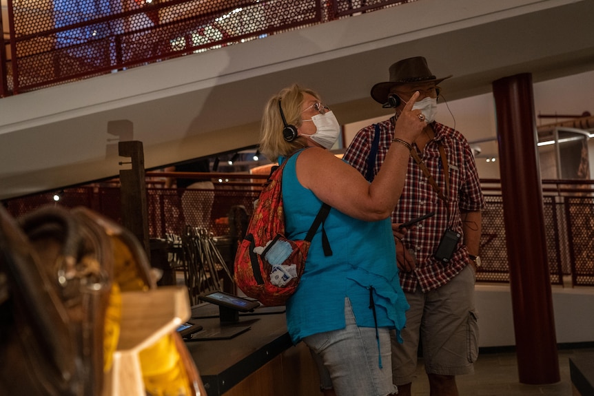 A man and a woman wearing masks and headsets point to something in a museum.