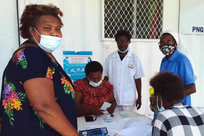 A PNG woman in a mask standing with others during a vaccination drive