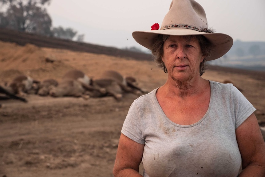 Kim Winter looks stern, wearing a white rimmed hat, dirty grey t-shirt, standing in front of dead cattle.