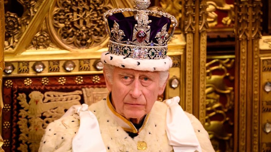 King Charles sits in crown and royal regalia on a throne 