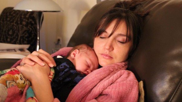 A woman sitting on a couch cuddling a newborn baby, both are asleep.