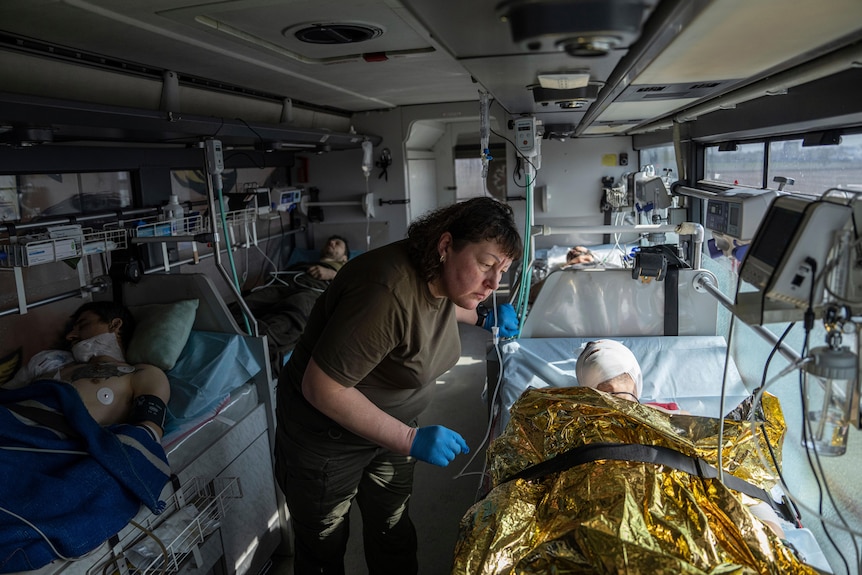 A volunteer speaks to a man laying on a bed with bandages over his face.