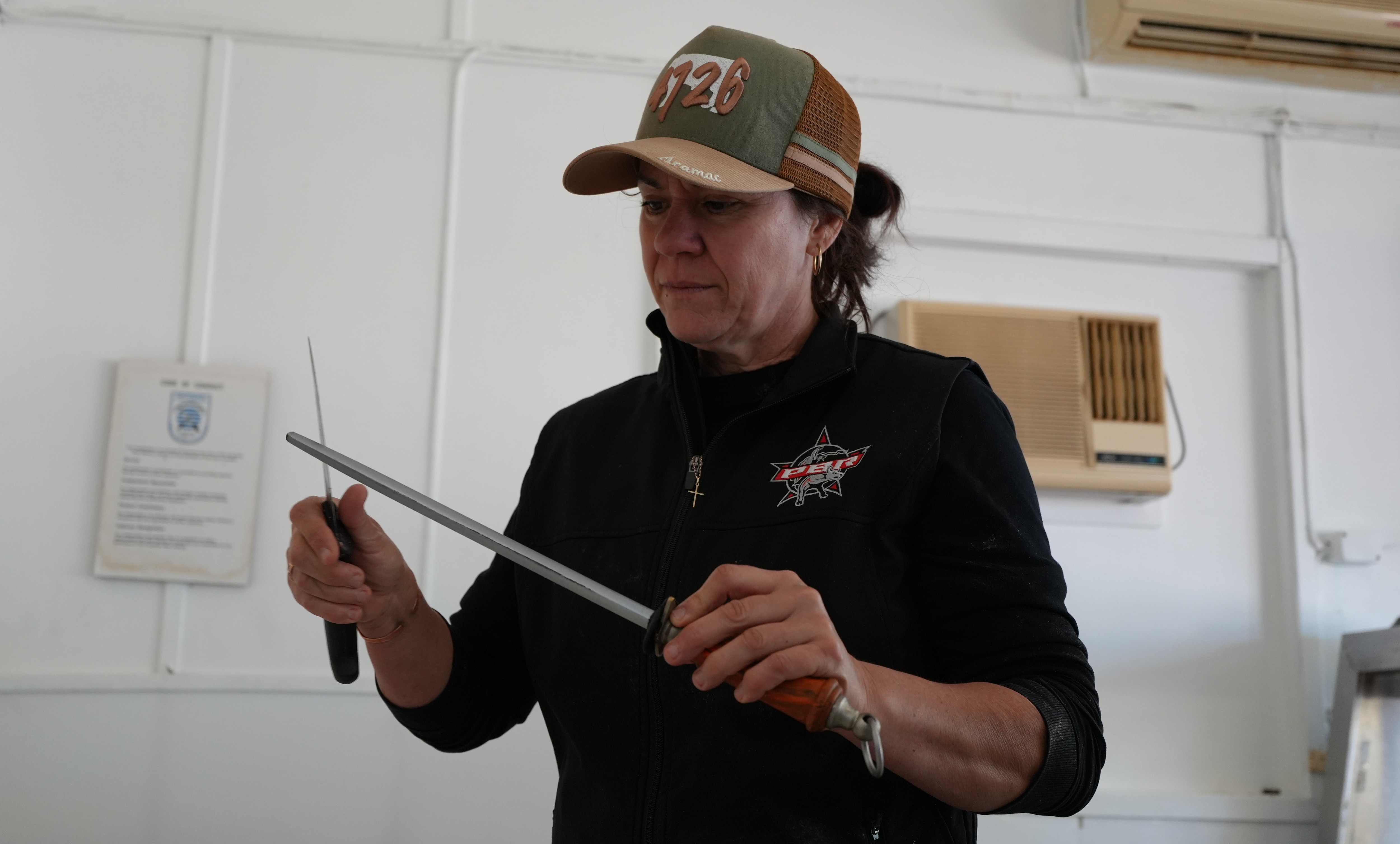 Female butcher sharpening knife on metal stick.
