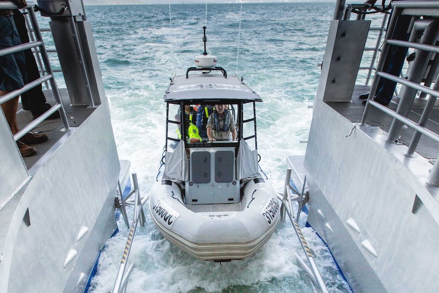 A small boat is lowered into the water from the stern of a larger boat, via a hydraulic platform.