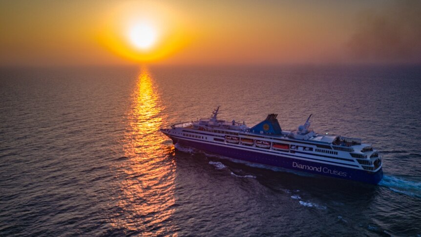 A cruise ship heads out to international waters towards a setting sun.