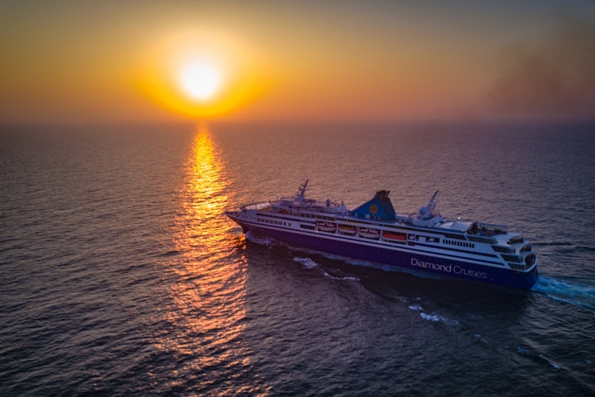 A cruise ship heads out to international waters towards a setting sun.