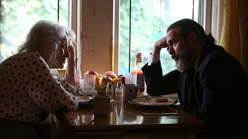 Joaquin Phoenix and Judith Roberts sit at a table in film You Were Never Really Here.