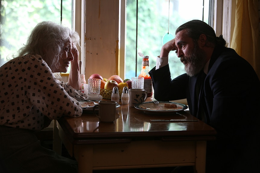 Joaquin Phoenix and Judith Roberts sit at a table in film You Were Never Really Here.
