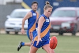 woman footballer in blue and gold jumper mid-kick