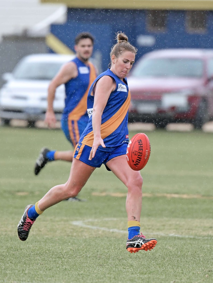 woman footballer in blue and gold jumper mid-kick