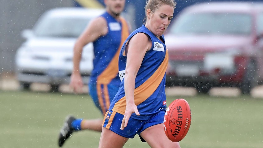 woman footballer in blue and gold jumper mid-kick