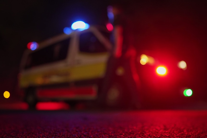 A non-identifiable paramedic walks next to an ambulance with its lights on