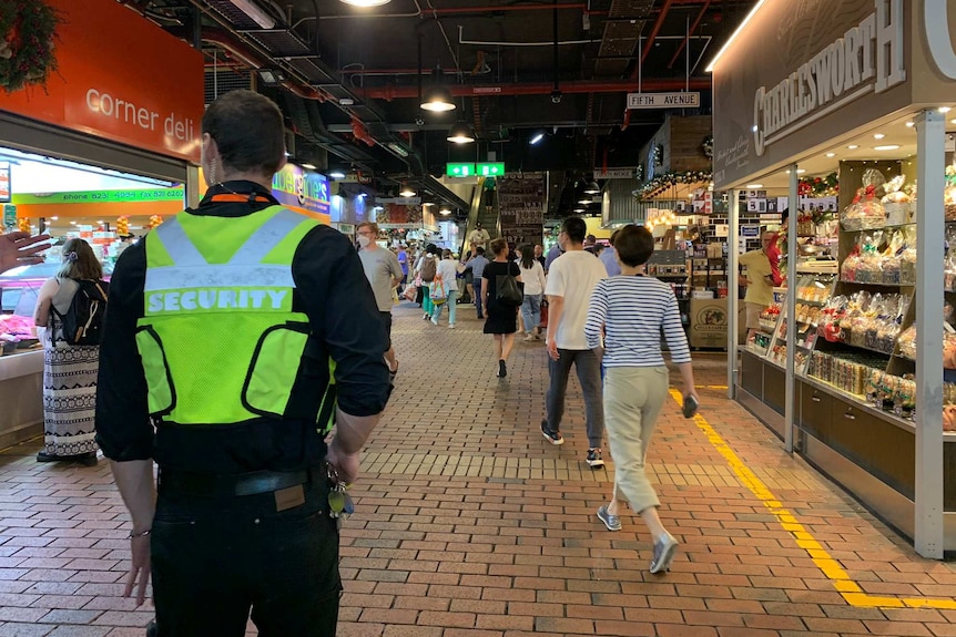 A security guard stands in the aisle of a market and a nut shop