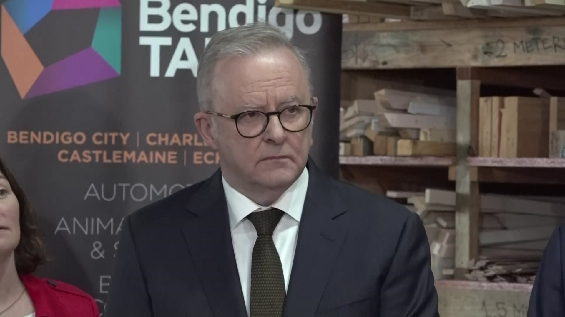 A man with short hair, wearing glasses and a suit and tie, looking serious.