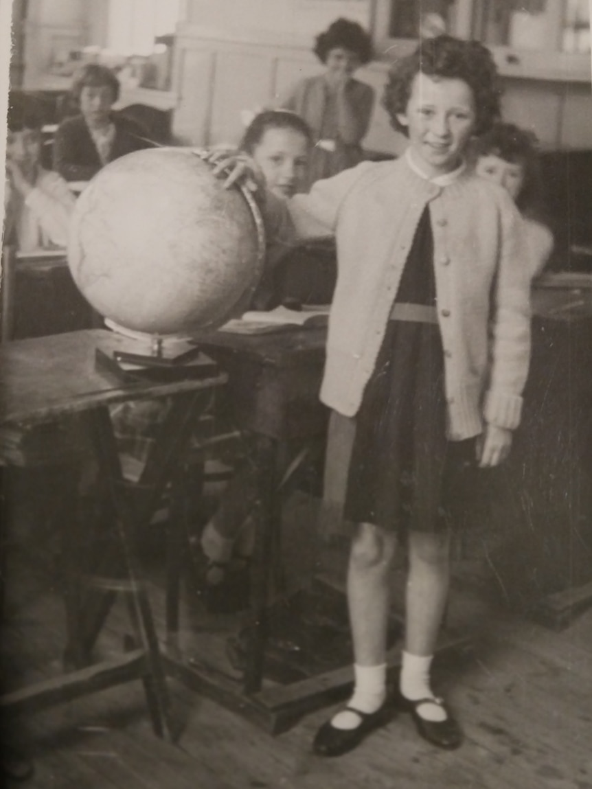 A young girl in a black and white photo points to a globe