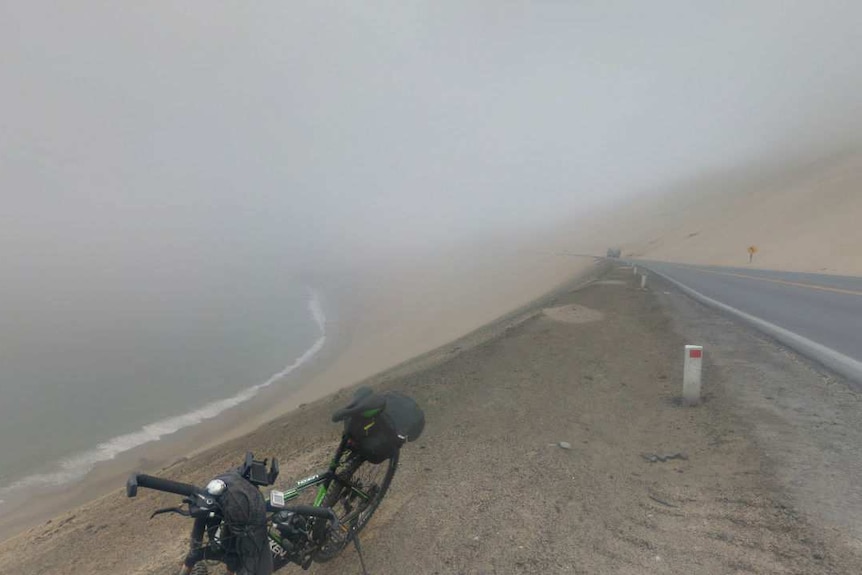 A bike stands in front of a misty highway and cliff.