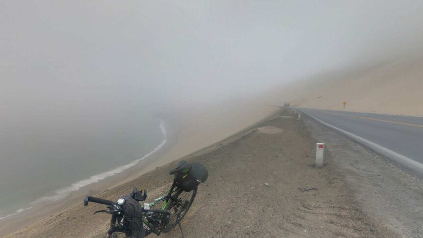A bike stands in front of a misty highway and cliff.