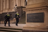 Two police officers wearing masks walk next to a Parliament of Victoria sign.