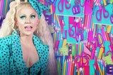 Courtney Act on the left, notebooks, pens and pencils in the background