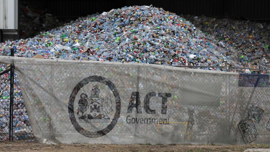 A huge pile of plastic bottles looms behind an ACT Government fence at a recycling centre in Hume.