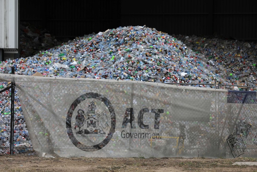 A huge pile of plastic bottles looms behind an ACT Government fence at a recycling centre in Hume.
