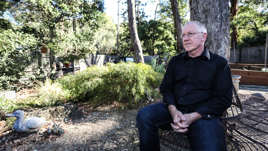 Melbourne Men's Group convenor David Mallard at home sitting in his back yard on a bench under a tree.