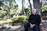 Melbourne Men's Group convenor David Mallard at home sitting in his back yard on a bench under a tree.
