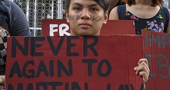 A young Filipino protester holds up a sign that reads "never again."