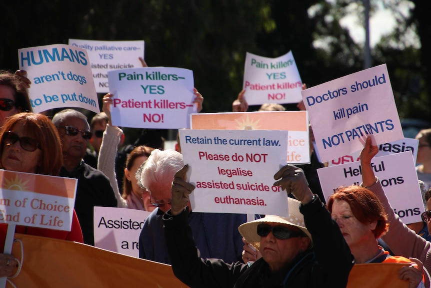 People hold signs opposing euthanasia at a rally.