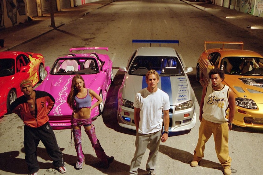 Devon Aoki and Paul Walker standing in front of race cars
