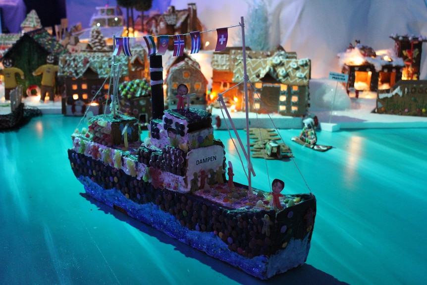 A model boat made from gingerbread and sweets sits on the mock water made from blue sheeting.