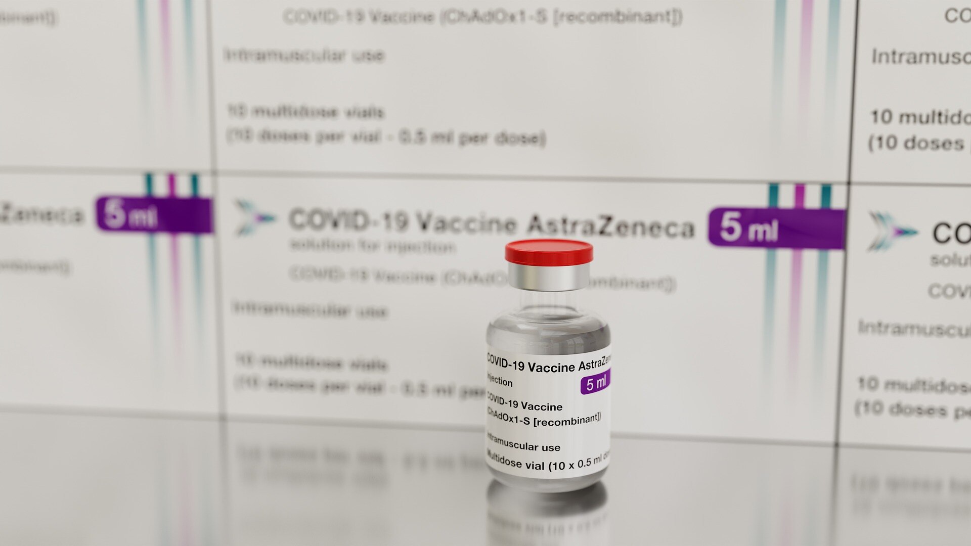 Single glass vial of AstraZeneca vaccine sits in front of multiple packages of the same vaccine.
