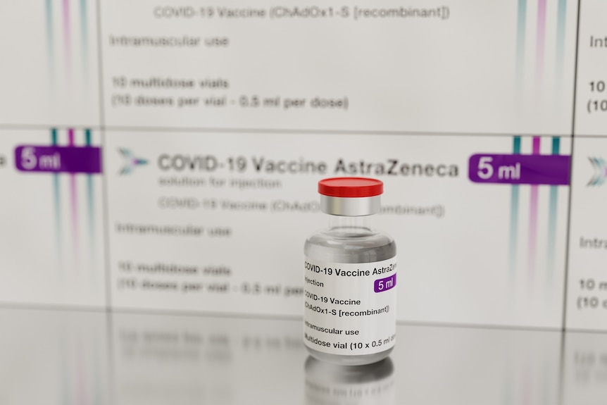 Single glass vial of AstraZeneca vaccine sits in front of multiple packages of the same vaccine.