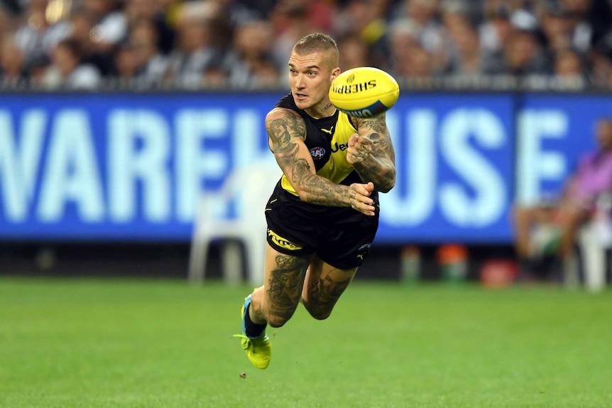 Dustin Martin dives in the air as he performs a handball.