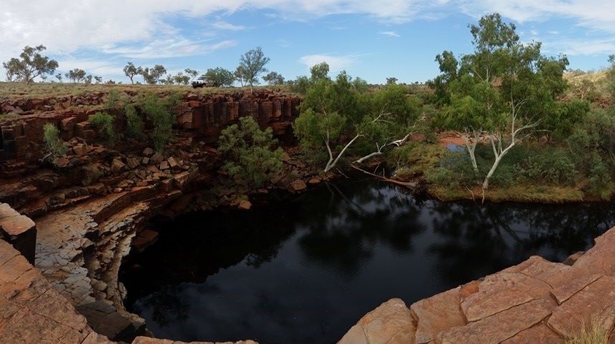 A waterhole at the bottom of a gorge surrounded by red rocks and gumtrees