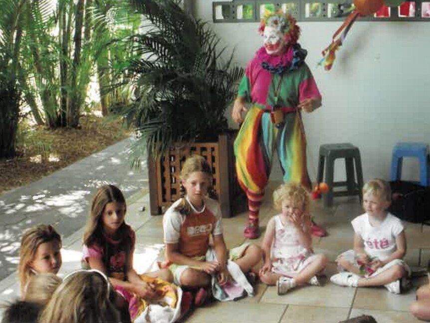 A clown entertaining a circle of seated small children.