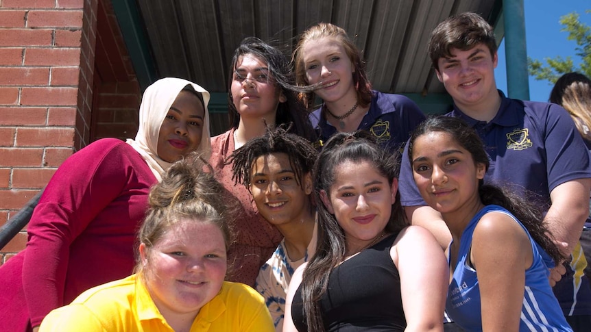 A group of students of varying appearances, including dark and light faces, one girl with a headscarf, others in school t-shirts