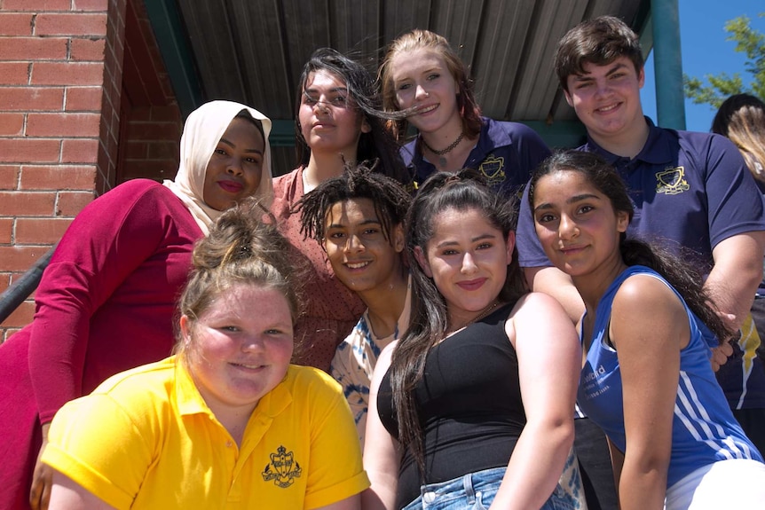 A group of students of varying appearances, including dark and light faces, one girl with a headscarf, others in school t-shirts
