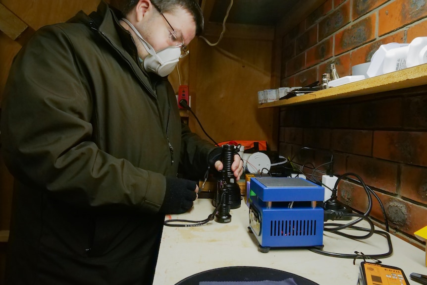 A man handling a torch on a workbench while wearing a COVID mask