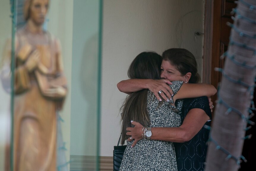 Two women hug tightly as they meet outside a funeral home.