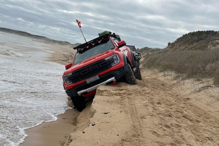 A red ute stuck on the side of a sandy embankment. 