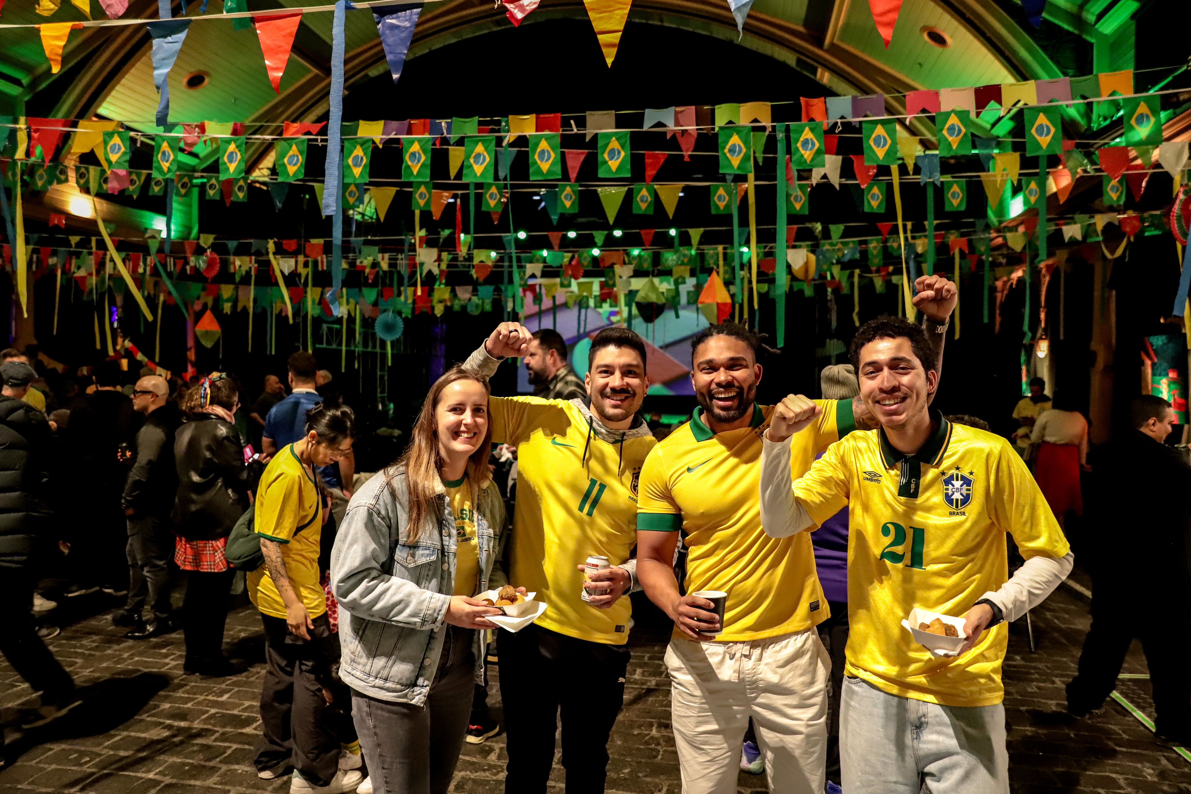 Three men and one woman wearing bright yellow and green Brazil outfits inside a dark event room full of people and decorations