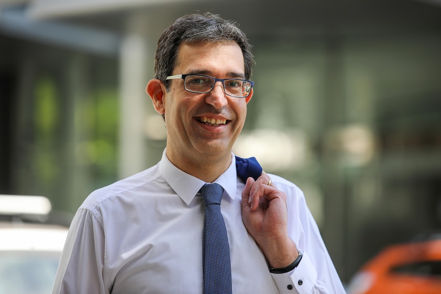 A man in a shirt and tie smiling. 