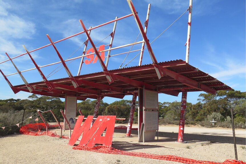 A large steel red sign on the WA/SA border. The letters SA are raised high on poles and the WA part of the sign has fallen down 