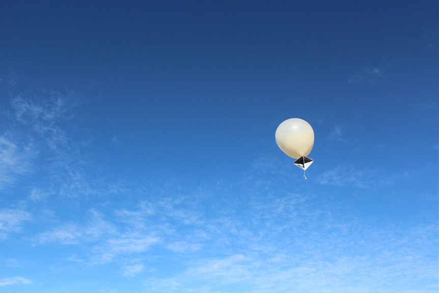 A silver weather balloon rising into the sky